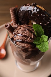 Photo of Delicious chocolate ice cream with wafer sticks, donut and mint in glass dessert bowl on table, closeup