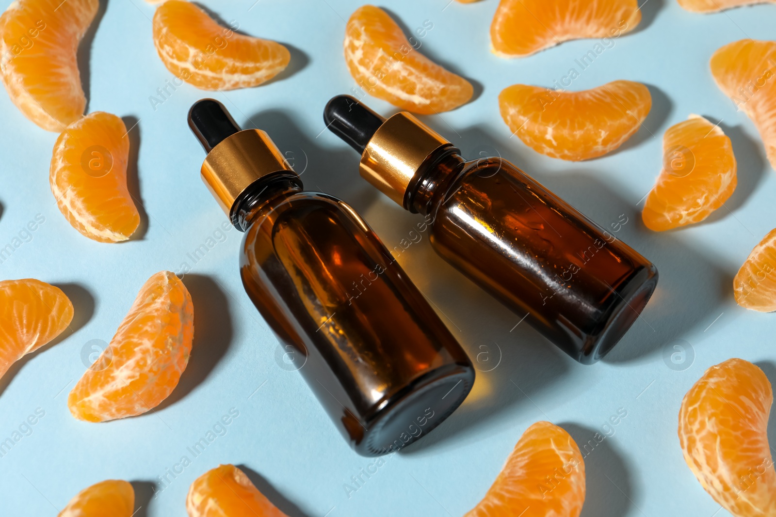 Photo of Aromatic tangerine essential oil in bottles and citrus fruits on light blue table, closeup