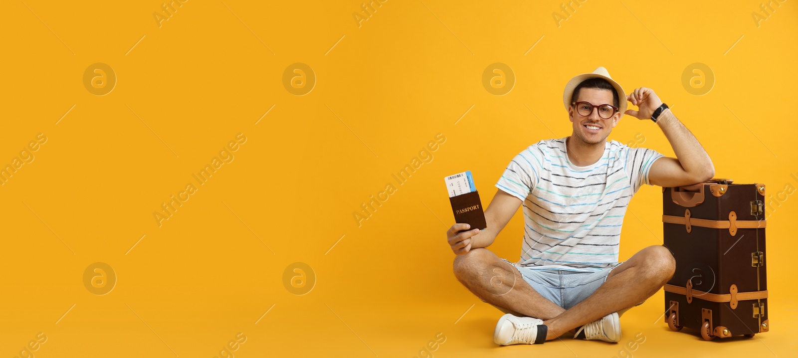 Photo of Male tourist holding passport with ticket near suitcase on yellow background