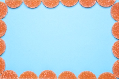 Photo of Frame made with orange marmalade candies on light blue background, flat lay. Space for text