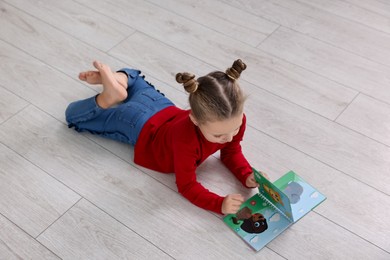 Photo of Cute little girl reading book on warm floor indoors. Heating system