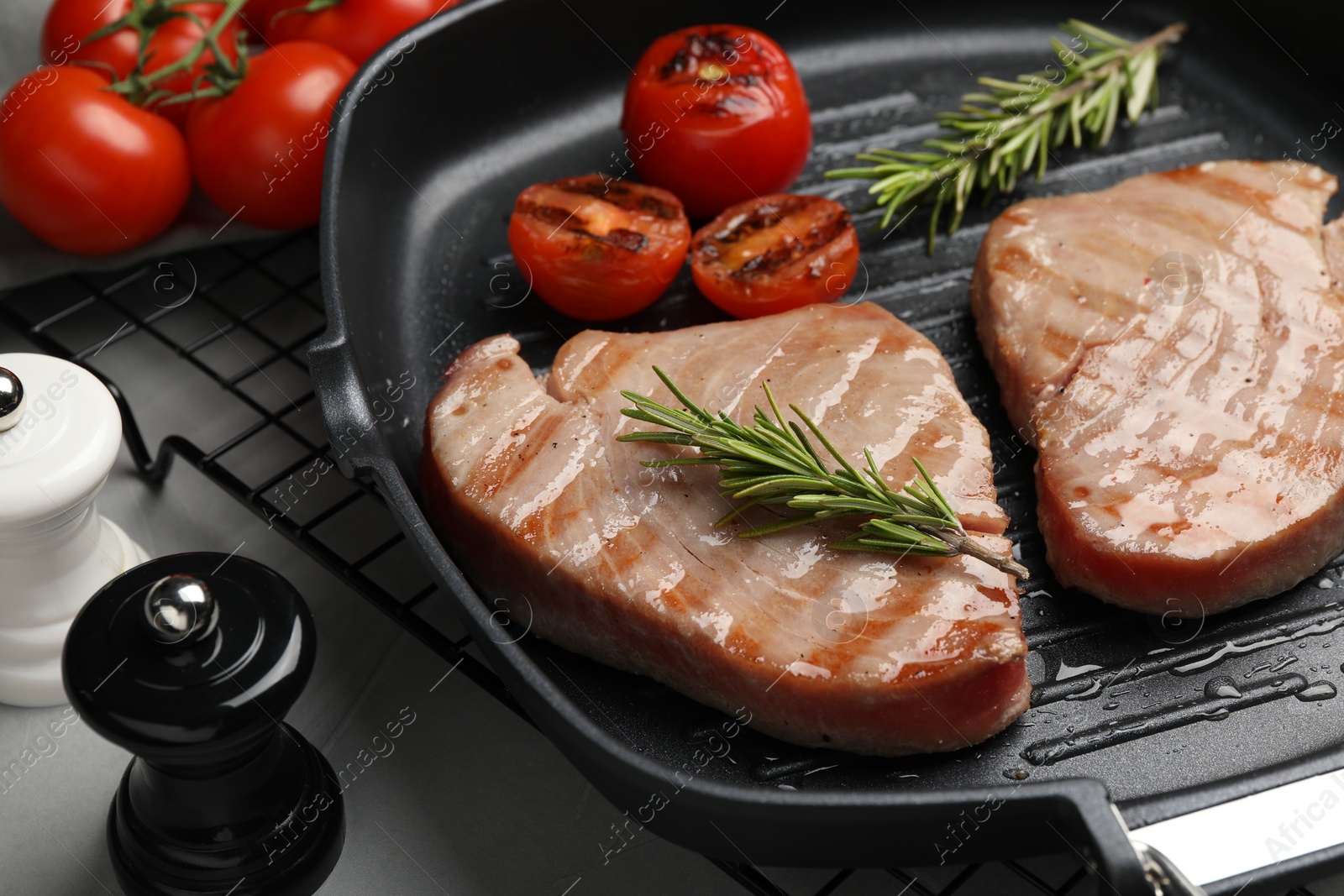 Photo of Delicious tuna steaks with rosemary and tomatoes on grey table, closeup