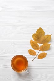 Photo of Small branch with autumn leaves and cup of delicious tea on white wooden table, flat lay