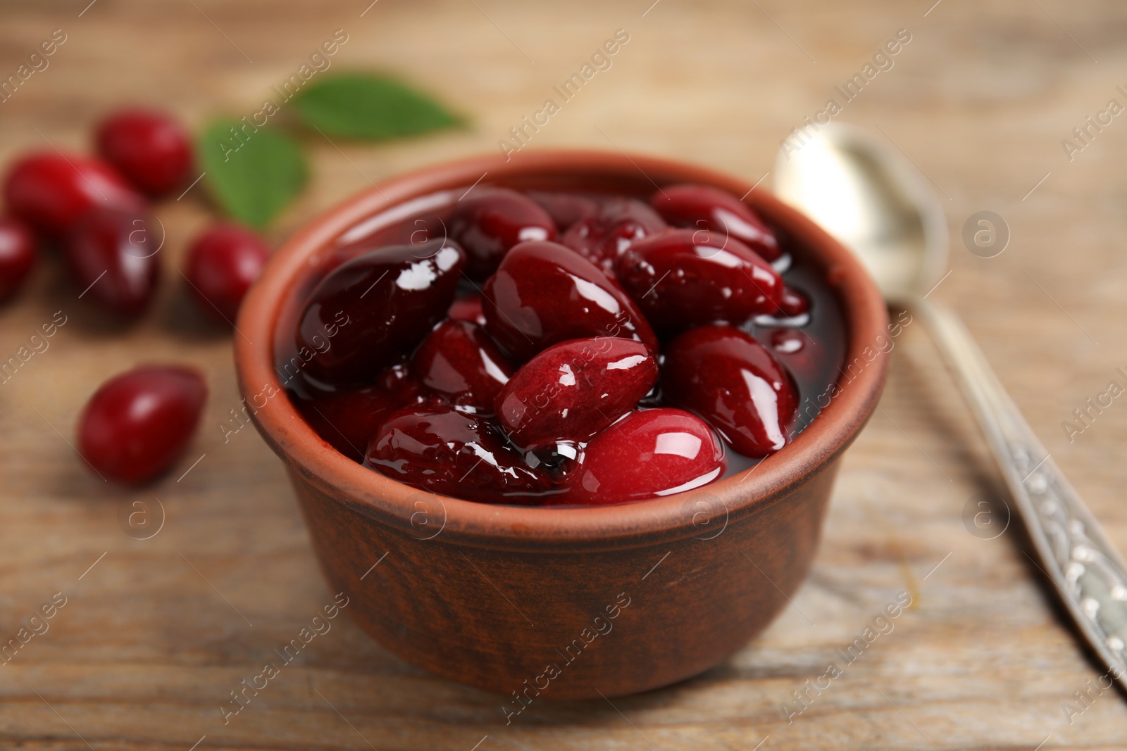 Photo of Delicious dogwood jam with berries in bowl on wooden table, closeup