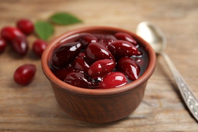 Photo of Delicious dogwood jam with berries in bowl on wooden table, closeup