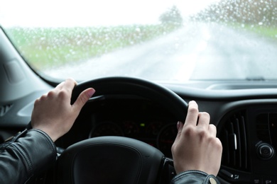 Woman driving car on rainy day, closeup of hands