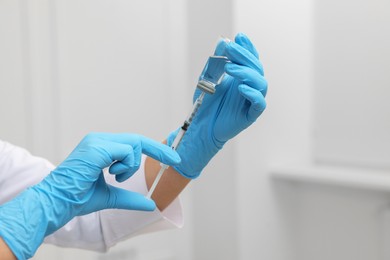 Photo of Doctor filling syringe with medication from glass vial indoors, closeup