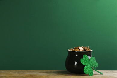 Photo of Pot of gold coins and clover on wooden table against green background, space for text. St. Patrick's Day celebration