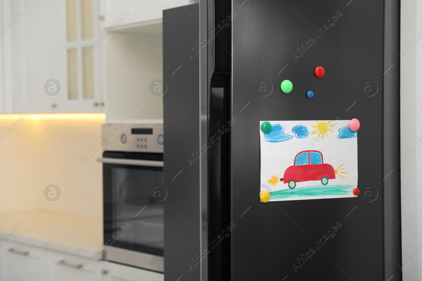 Photo of Modern refrigerator with child's drawing and magnets in kitchen