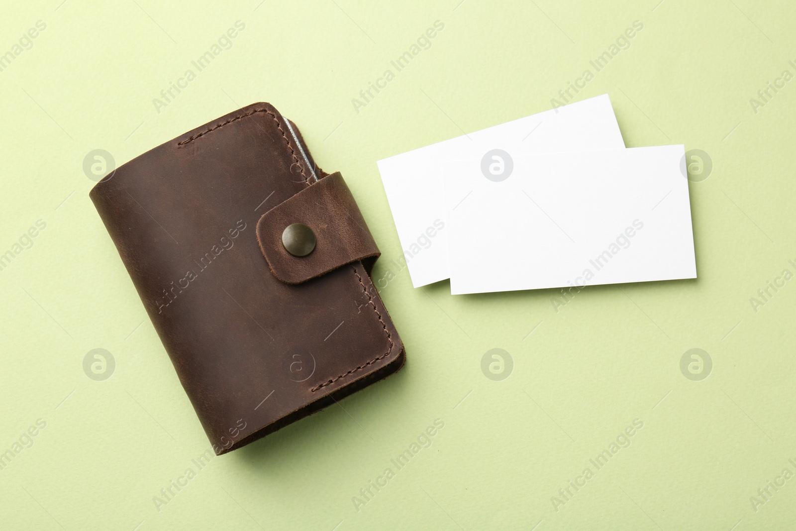 Photo of Leather business card holder with blank cards on light green background, top view