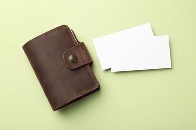 Leather business card holder with blank cards on light green background, top view