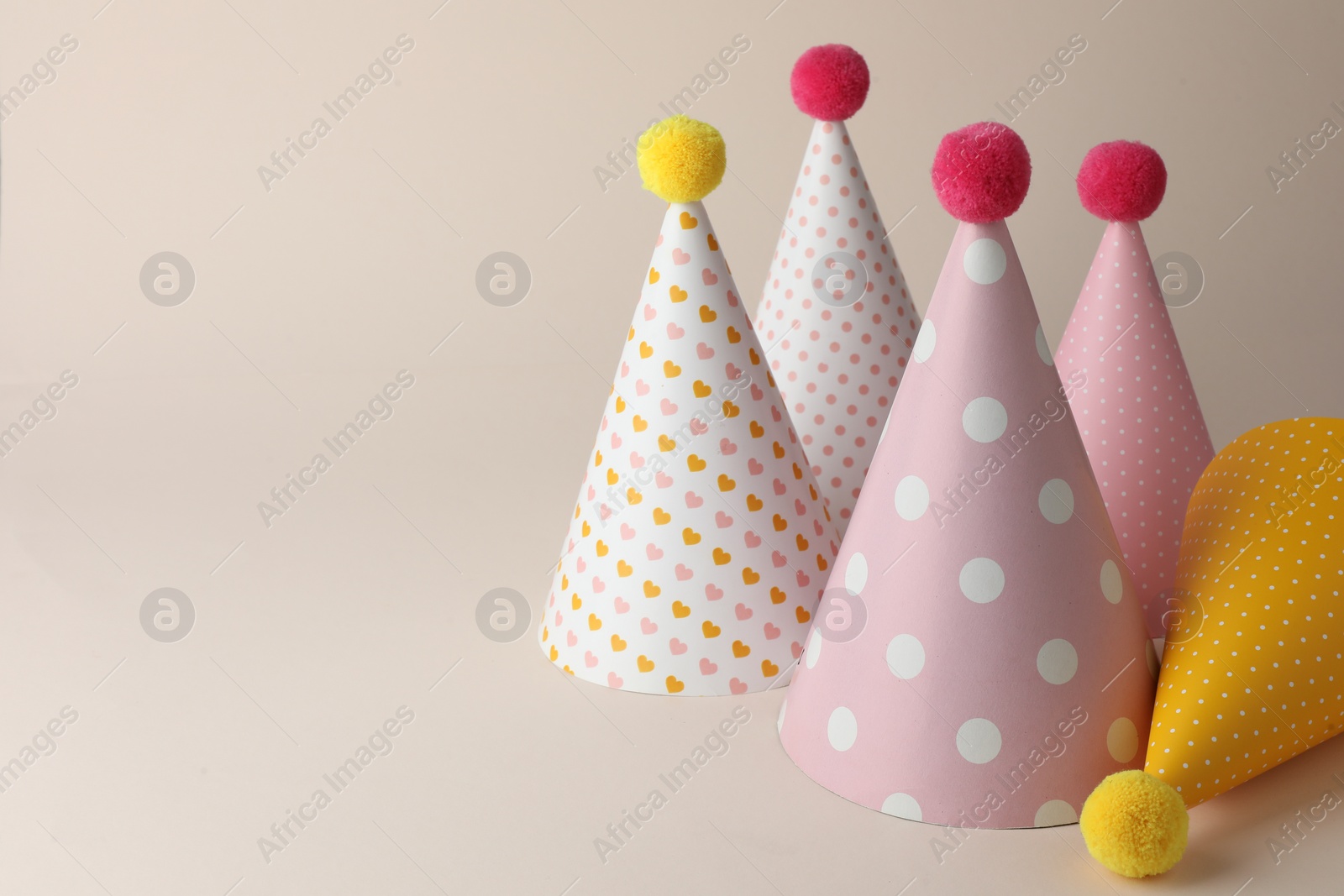 Photo of Beautiful party hats with pompoms on beige background. Space for text