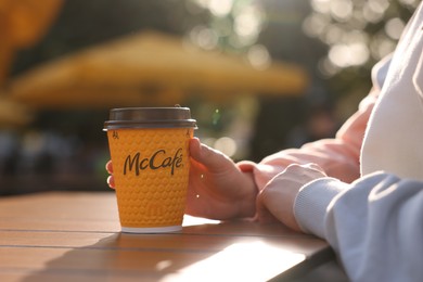 Photo of Lviv, Ukraine - September 26, 2023: Woman with hot McDonald's drink at wooden table outdoors, closeup