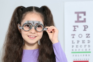 Little girl with trial frame near eye chart in hospital, space for text. Visiting children's doctor