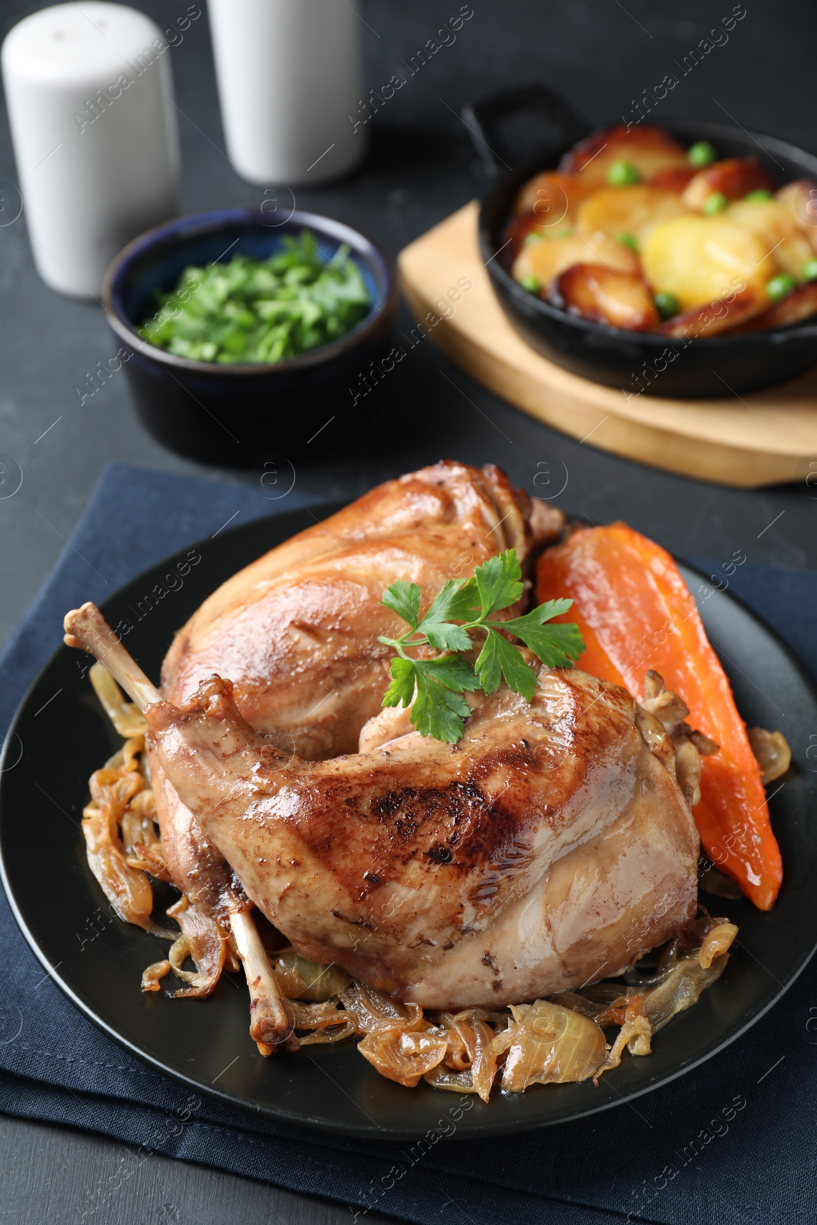 Photo of Tasty cooked rabbit meat with vegetables served on black table