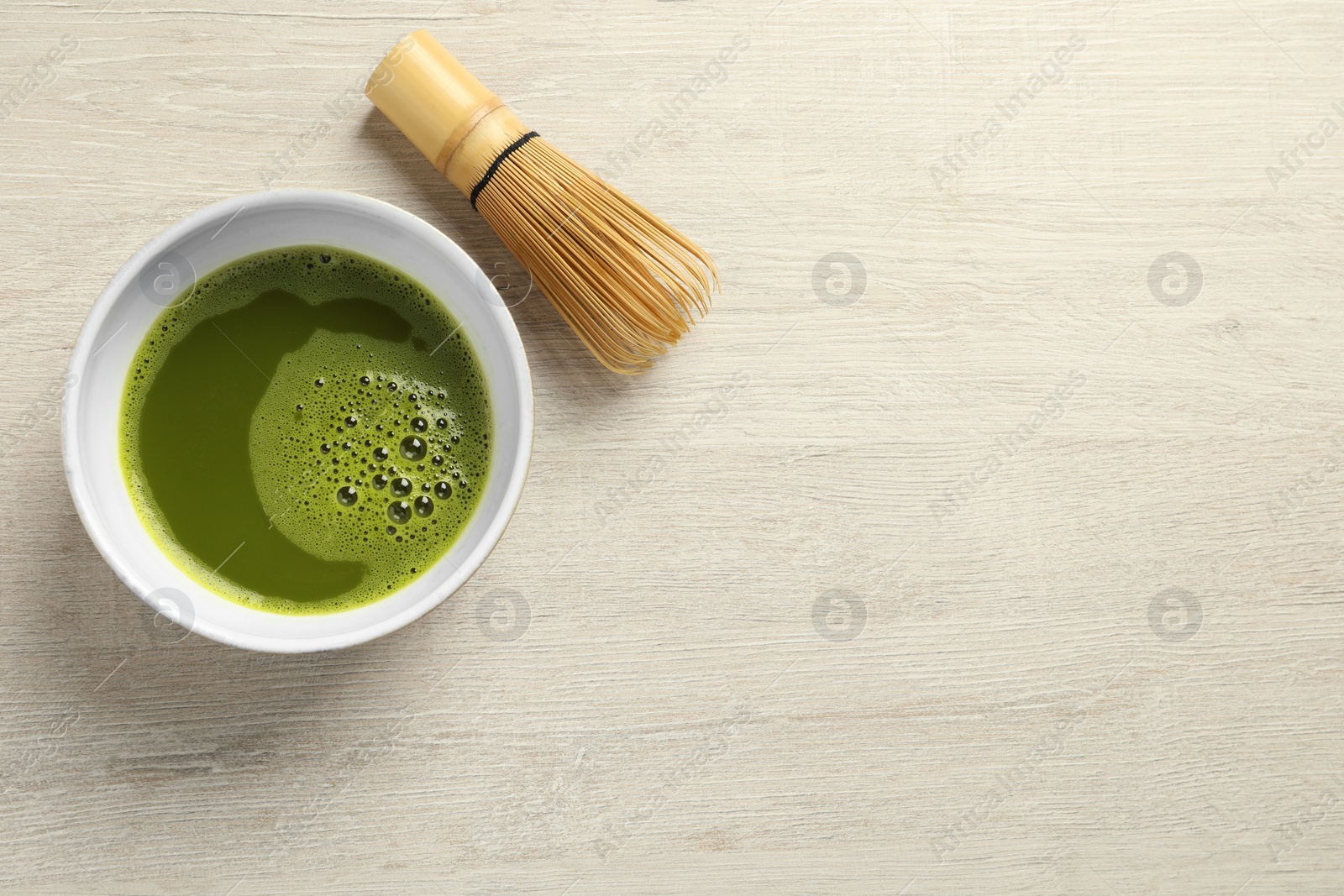 Photo of Cup of fresh matcha tea and bamboo whisk on white wooden table, flat lay. Space for text