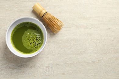 Photo of Cup of fresh matcha tea and bamboo whisk on white wooden table, flat lay. Space for text