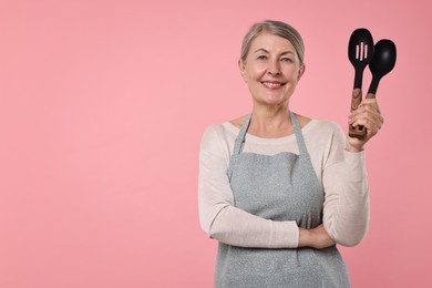 Happy housewife with spoons on pink background, space for text
