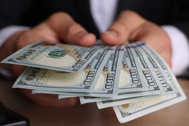 Money exchange. Man counting dollar banknotes at wooden table, closeup