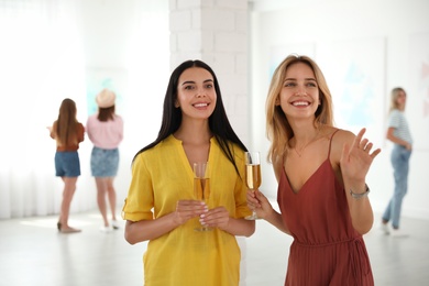 Young women with glasses of champagne at exhibition in art gallery