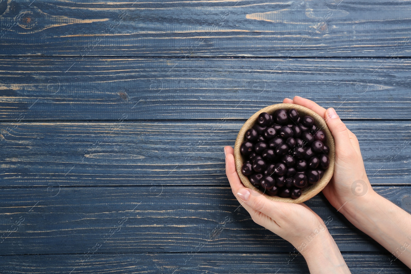 Photo of Woman holding bowl with tasty acai berries at blue wooden table, top view. Space for text