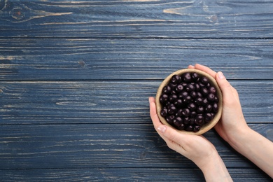 Photo of Woman holding bowl with tasty acai berries at blue wooden table, top view. Space for text