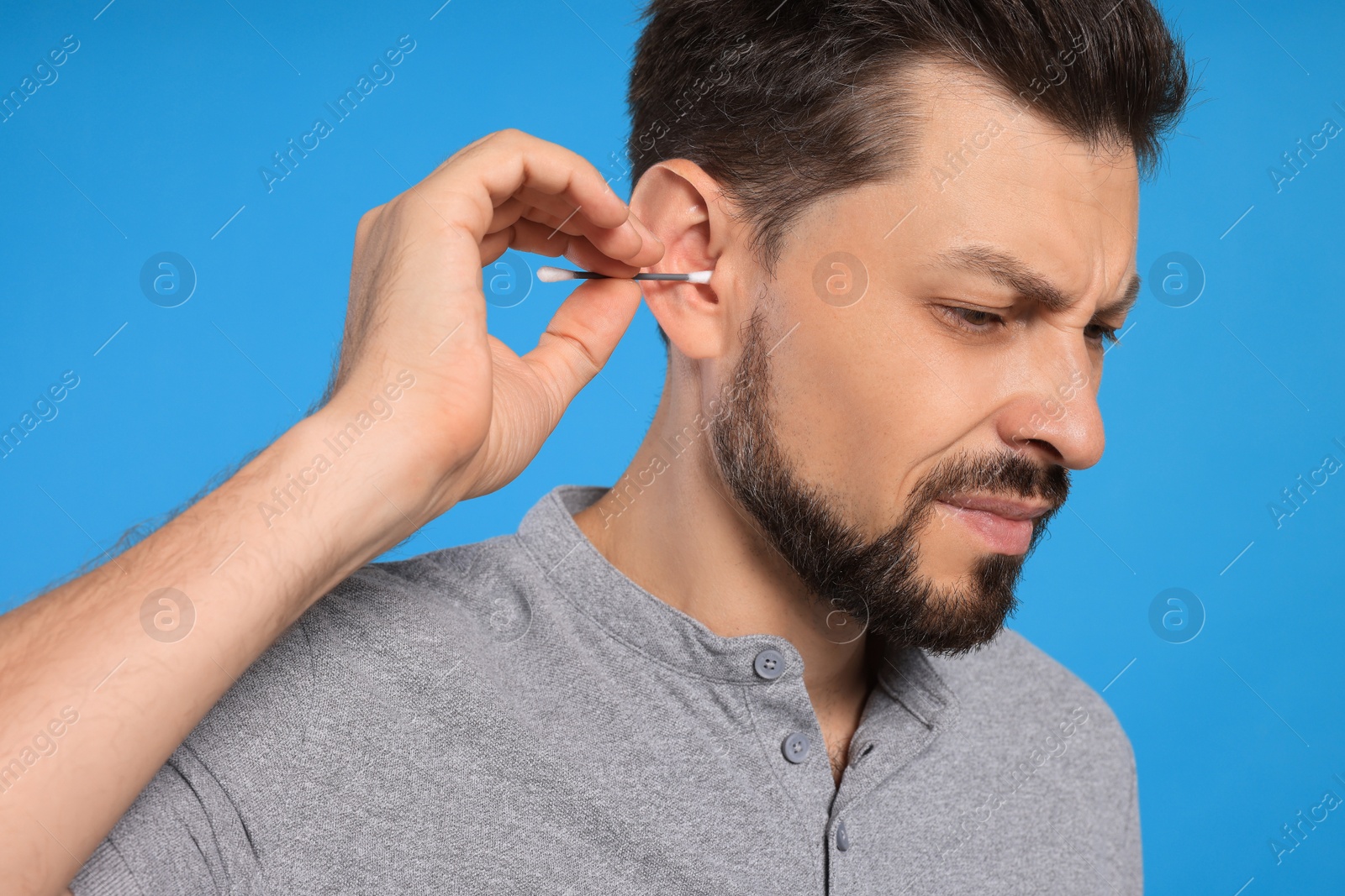 Photo of Emotional man cleaning ears on light blue background