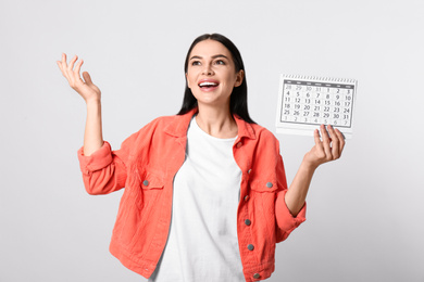 Photo of Emotional young woman holding calendar with marked menstrual cycle days on light background
