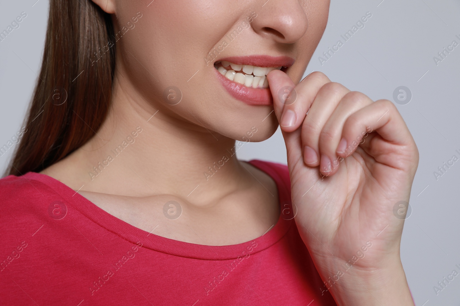 Photo of Young woman biting her nails on light grey background, closeup