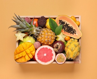 Crate with different exotic fruits on yellow background, top view