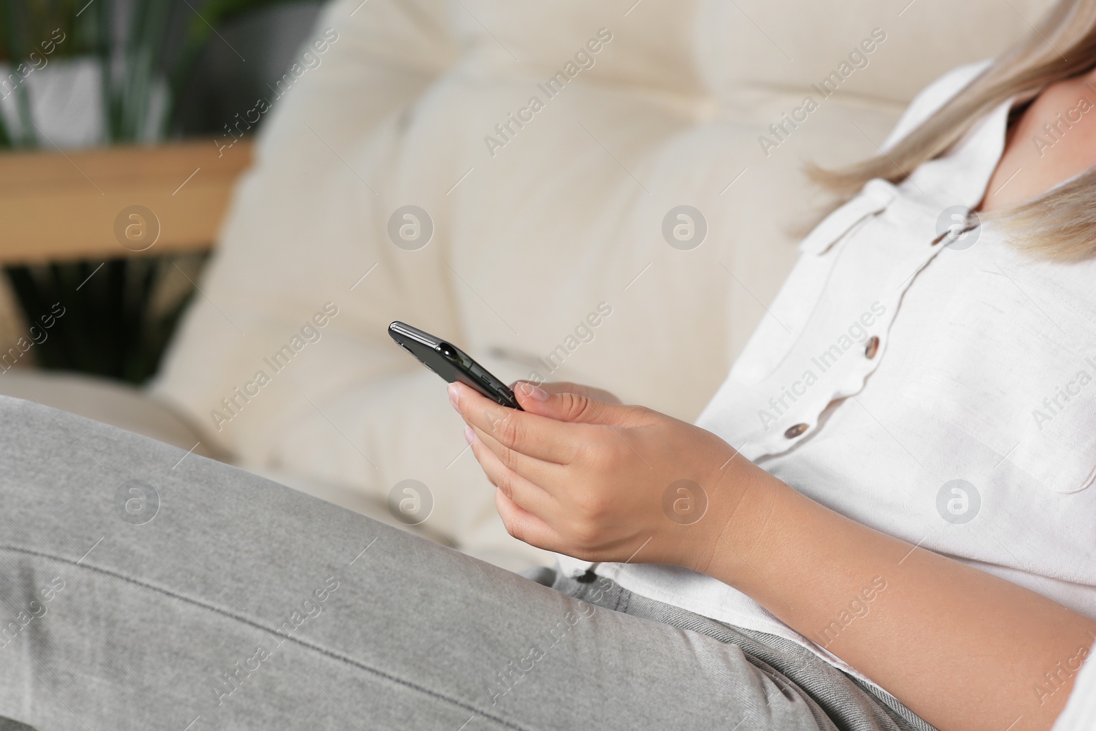 Photo of Woman using smartphone on sofa at home, closeup