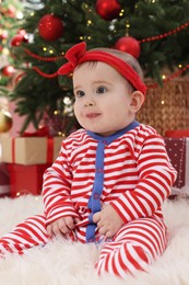 Baby wearing bright Christmas pajamas on floor in room