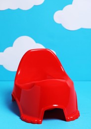 Red baby potty against light blue background with paper clouds. Toilet training