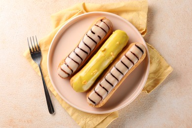 Different tasty glazed eclairs served on color textured table, top view