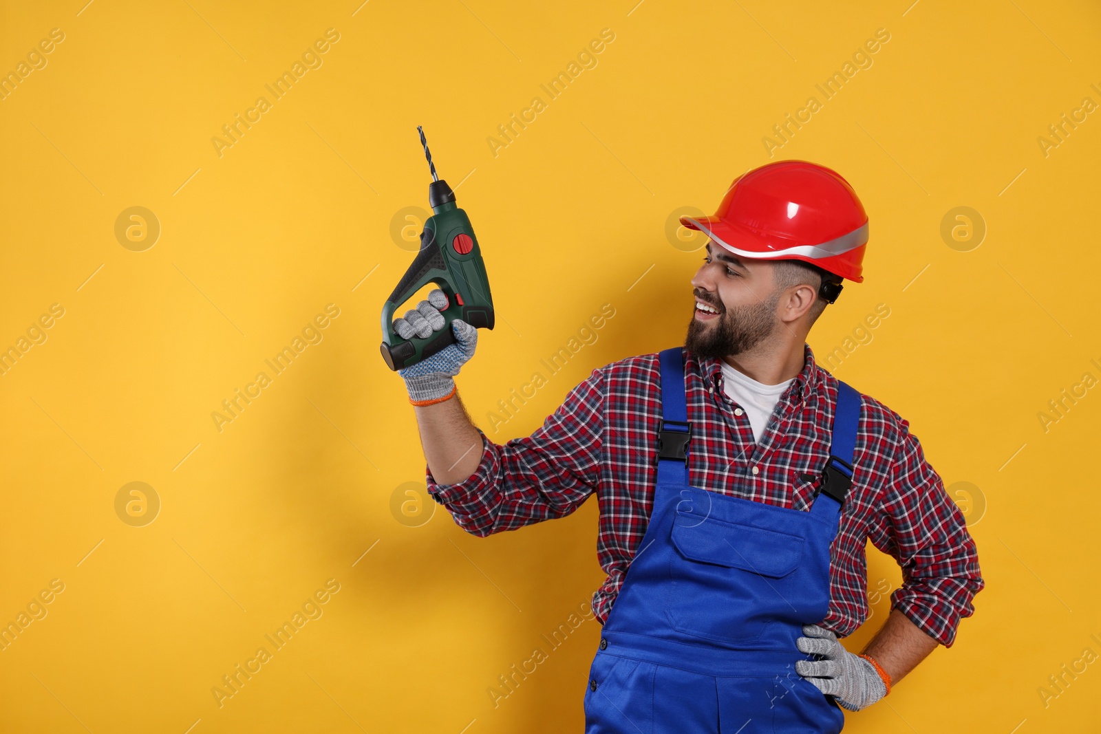 Photo of Young worker in uniform with power drill on yellow background. Space for text