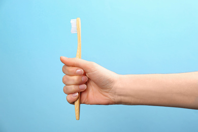 Photo of Woman holding bamboo toothbrush on light blue background, closeup