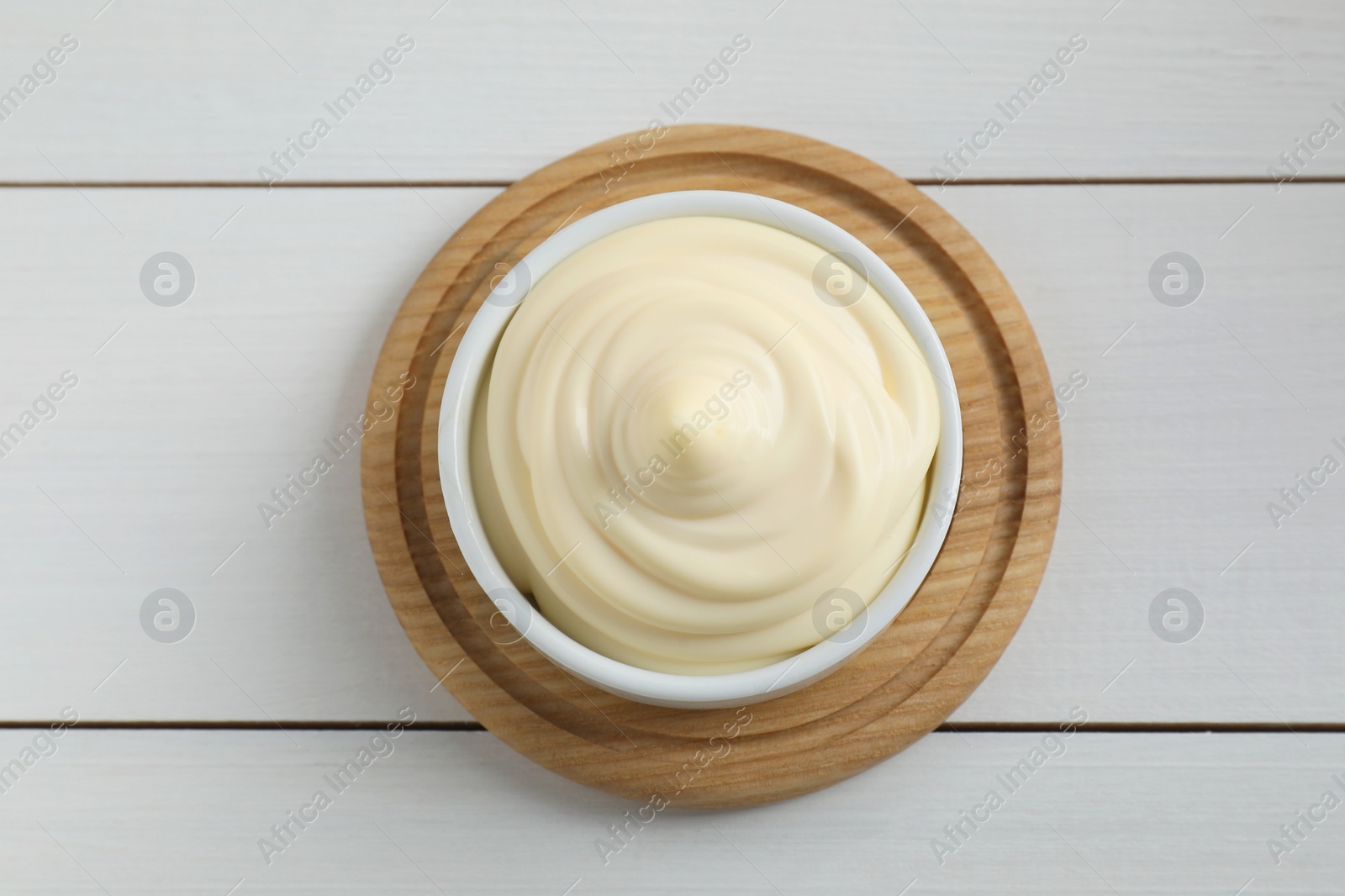 Photo of Fresh mayonnaise sauce in bowl on white wooden table, top view