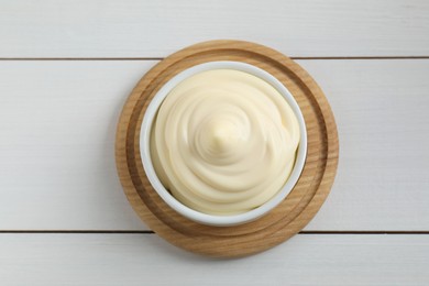 Fresh mayonnaise sauce in bowl on white wooden table, top view