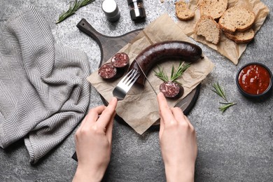 Woman eating tasty blood sausage at grey table, top view
