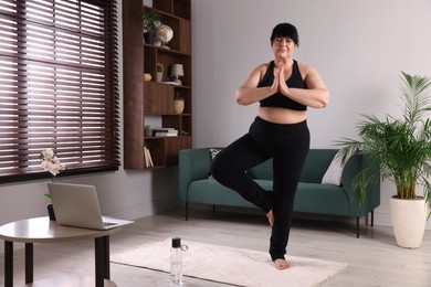 Photo of Overweight mature woman practicing yoga on rug at home