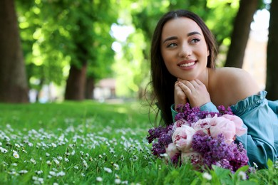 Photo of Beautiful woman with bouquet of spring flowers on green grass in park, space for text