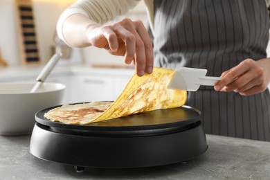 Photo of Woman cooking delicious crepe on electric pancake maker in kitchen, closeup