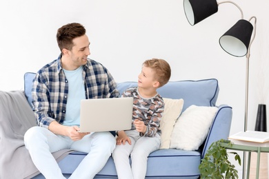 Photo of Dad and his son with laptop sitting on sofa at home