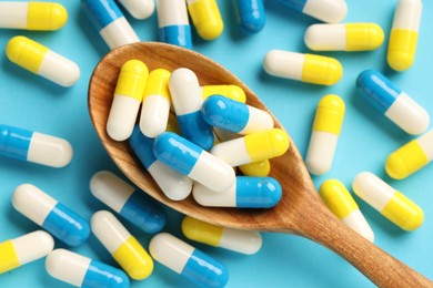 Photo of Many antibiotic pills with wooden spoon on light blue background, top view. Medicinal treatment