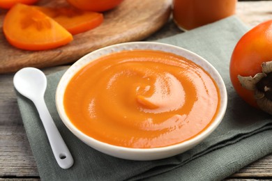 Delicious persimmon jam and fresh fruits on wooden table, closeup