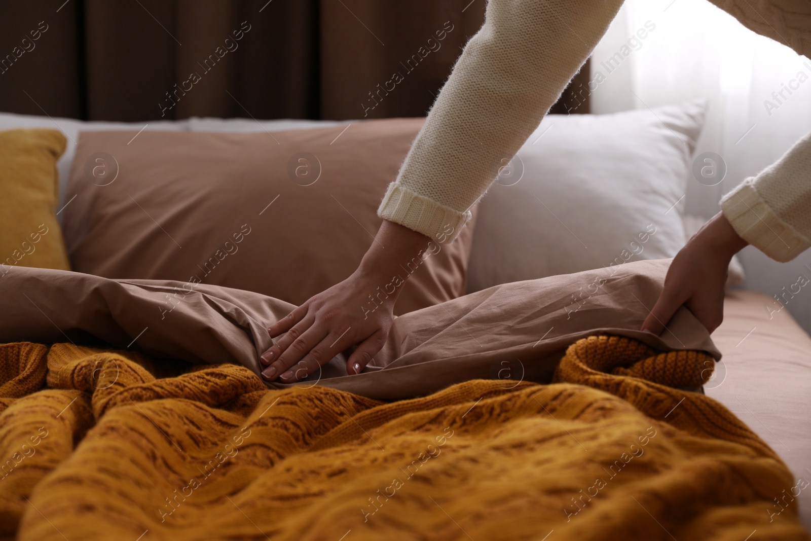 Photo of Woman making bed with brown linens, closeup