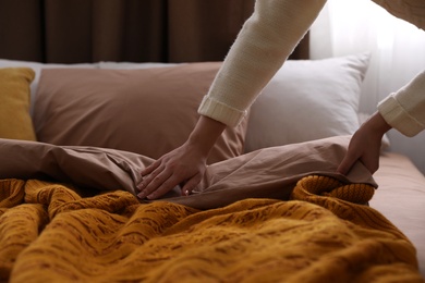 Woman making bed with brown linens, closeup