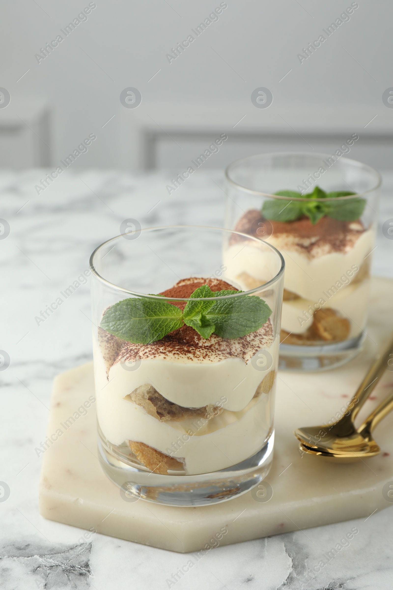 Photo of Delicious tiramisu in glasses, mint leaves and spoons on white marble table