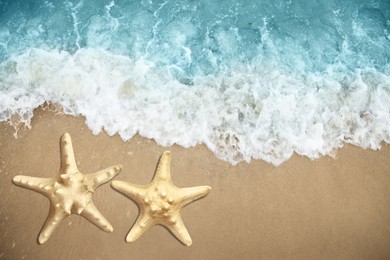 Image of Beautiful waves and sea stars on sandy beach, top view