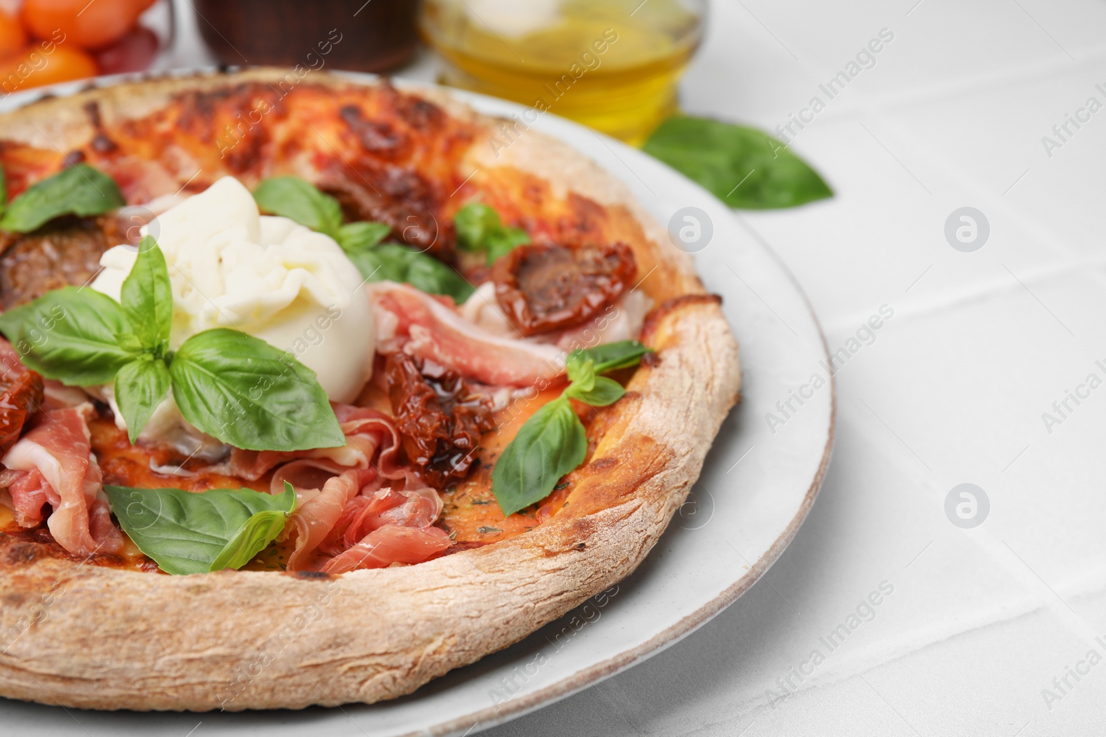 Photo of Delicious pizza with burrata cheese, basil, ham and sun-dried tomatoes on white tiled table, closeup. Space for text